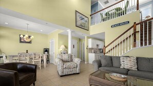 A spacious living area with a dining table, two sofas, a coffee table, and a staircase leading to a second floor. - Pelican Perch - 3 bed/ den on water with boat dock and outdoor pool - 36th St area sleeps 10 (Ocean City)