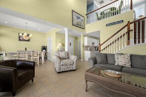 A spacious living area with a dining table, two sofas, a coffee table, and a staircase leading to a second floor. - Pelican Perch - 3 bed/ den on water with boat dock and outdoor pool - 36th St area sleeps 10 (Ocean City)