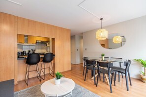 Une cuisine moderne avec des meubles en bois, un coin repas dot é d’une table en verre et de chaises noires, et un miroir rond accroché au mur.