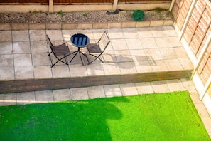Eine Terrasse mit kleinem Tisch und Stühlen, einem grünen Rasen und einer Ziegelwand.