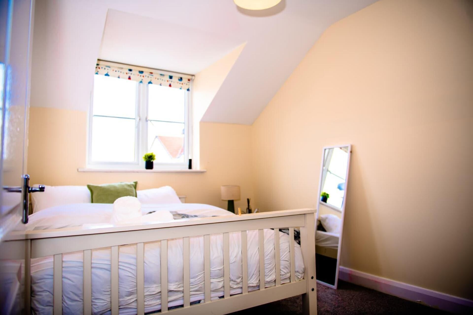 Une chambre avec un lit simple, une fenêtre avec des rideaux, une lampe de chevet et un miroir au mur.