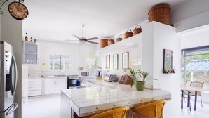 Une cuisine moderne avec des meubles blancs, un îlot central et un coin repas doté de chaises jaunes.