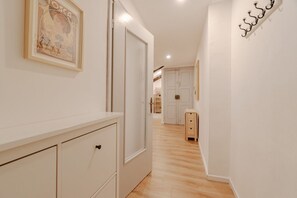Ein Flur mit weißer Wand, einem gerahmten Bild, einer Tür und einem Kleiderständer.