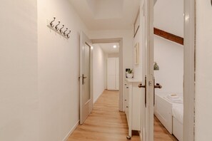 Ein schmaler Flur mit weißen Wänden und Holzboden, der in ein Schlafzimmer mit Bett und Nachttisch führt.