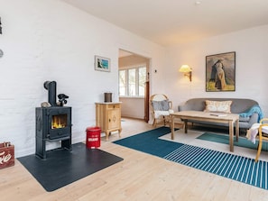 A cozy living room with a wood-burning stove, a sofa, a table, and a painting on the wall. - 6 Person Holiday Home in Stege (Stege)