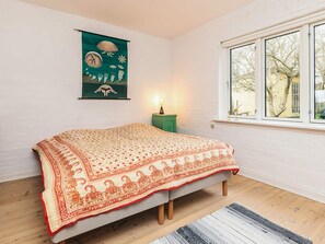 A bedroom with a bed, a nightstand, a lamp, a window, and a wall with a poster. - 6 Person Holiday Home in Stege (Stege)