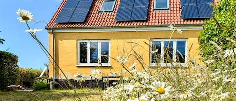 A house with a yellow facade, red-tiled roof, and solar panels.