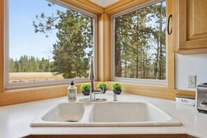 A kitchen with a double sink, wooden cabinets, a window with a view of trees, and a toaster.