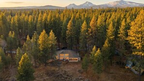Una casa envoltada d'un bosc dens amb una muntanya al fons.