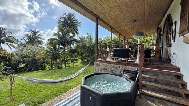 Een overdekt buitengebied met een hottub, een hangmat en een terras met tuinmeubilair.