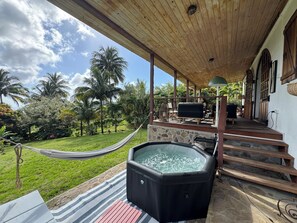 Un espace extérieur abrité comprenant un jacuzzi, un hamac et une terrasse avec mobilier d’extérieur.