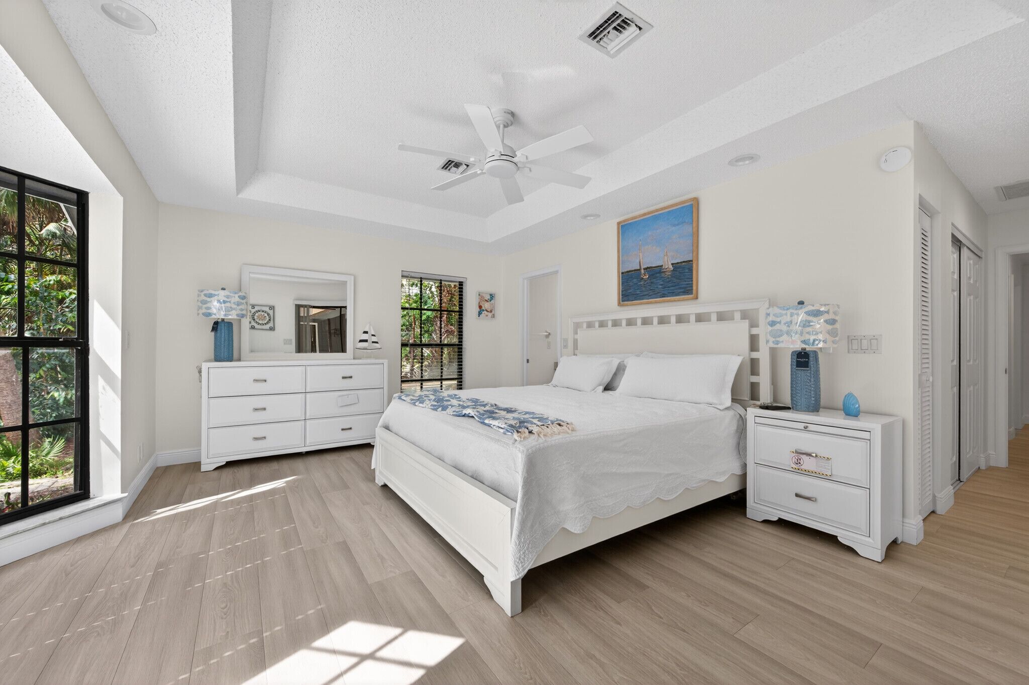 Une chambre à coucher comprenant un lit, des tables de chevet, une commode, un ventilateur de plafond et une fenêtre donnant sur un paysage verdoyant.
