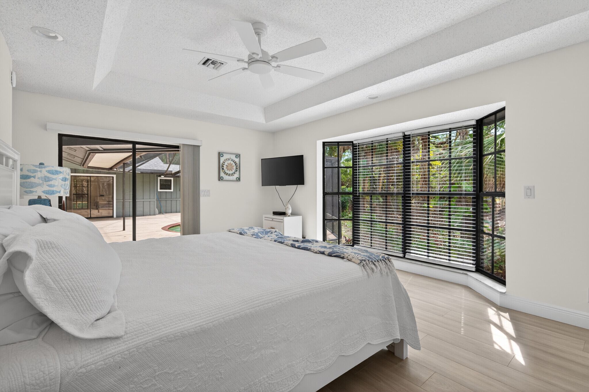 A bedroom with a large bed, a ceiling fan, a TV, and a window with blinds.