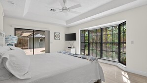 Ein Schlafzimmer mit einem großen Bett, einem Deckenventilator, einem Fernseher und einem Fenster mit Jalousien.