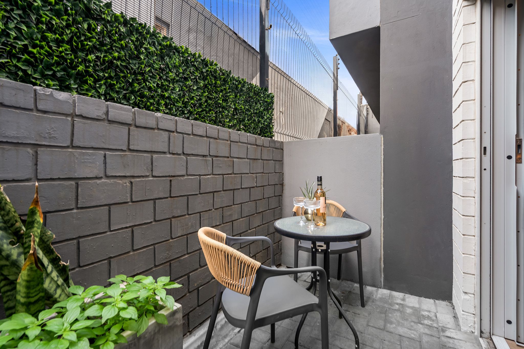 Un petit espace extérieur aménagé avec une table et deux chaises, une bouteille de vin et un verre.