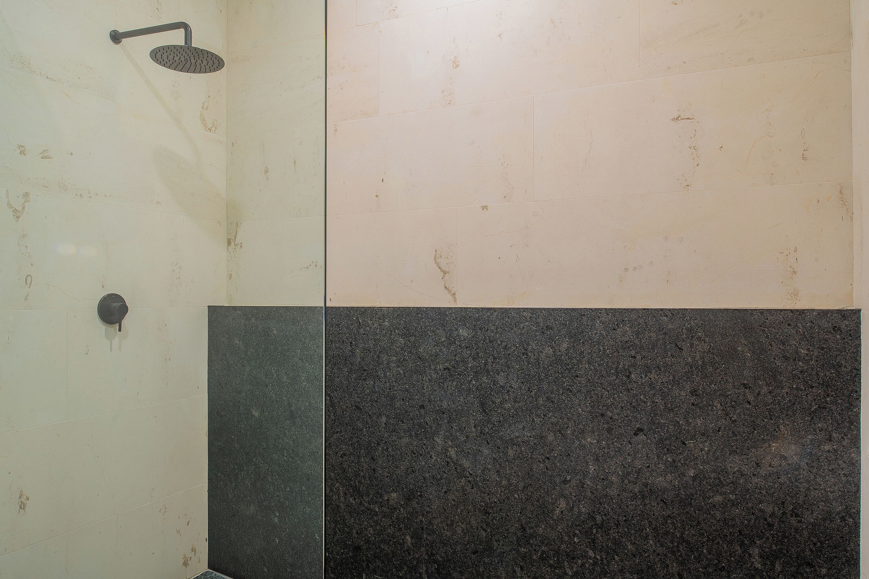 Een badkamer met een douche en twee soorten tegels: een lichte en een donkere.
