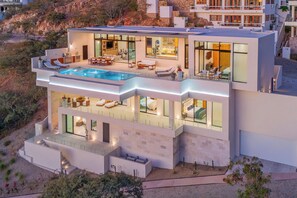 A modern multi-story house with a rooftop pool, large glass windows, and outdoor seating areas. - Luxury Villa w/ Pool, Butler, Walk to Swimmable Beach & Town w/ Ocean Views Cabo (Cabo San Lucas)