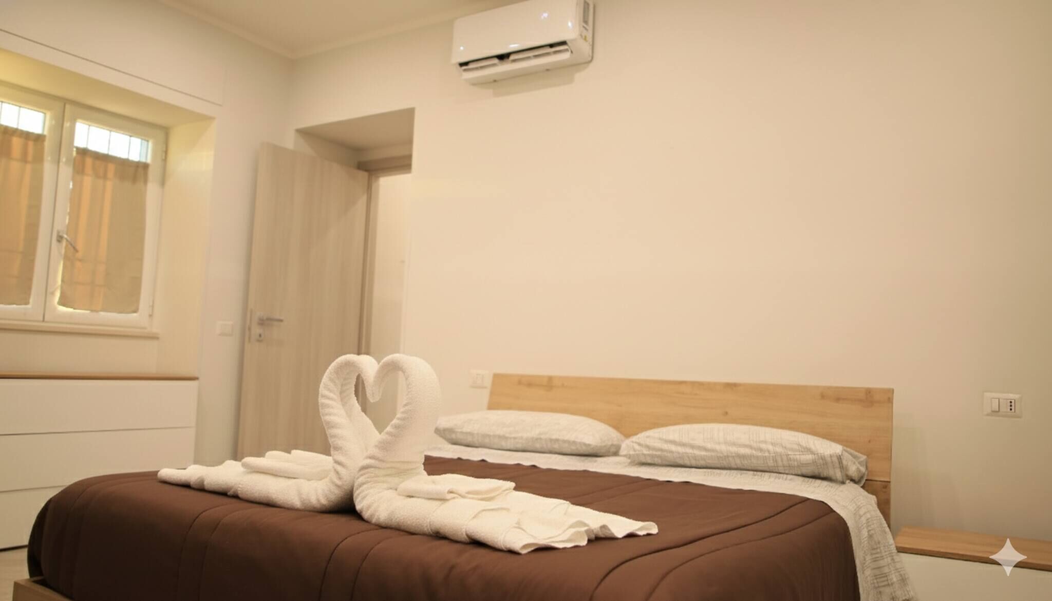 Une chambre d’hôtel avec un lit, une tête de lit en bois, une fenêtre avec des rideaux et un appareil de climatisation.