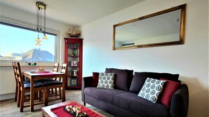 Ein Wohnzimmer mit einer Couch, einem Esstisch mit Stühlen, einem Bücherregal und einem großen Spiegel an der Wand.