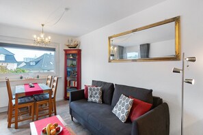 Una sala de estar con un sofá oscuro, una estantería roja, una mesa de comedor con sillas y un espejo grande en la pared.