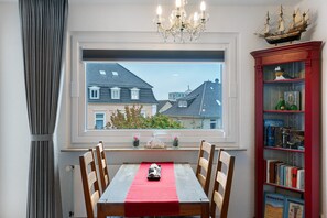 En matplats med ett bord dukat för två personer, ett fönster med utsikt över hus och en bokhylla med böcker och en modell av ett skepp.