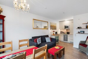 Ein modernes Wohnzimmer mit einer Couch, einem Esstisch, Stühlen und einer Küchenzeile mit Geräten.
