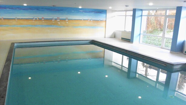 Ein überdachter Pool mit Fliesenboden und Blick auf den Strand durch die Wand.