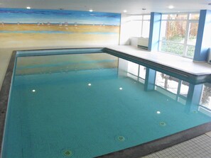 Una piscina interior con suelo de baldosas y vistas a la playa a través de la pared.