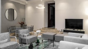 A modern living room with grey sofas, a glass coffee table, a flat-screen TV, and a staircase leading to another level. - Clayhall By SRS (Lagos)