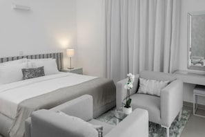 A modern hotel room with a large bed, a sitting area with a sofa and armchairs, a desk with a lamp, and a large window with curtains. - Clayhall By SRS (Lagos)