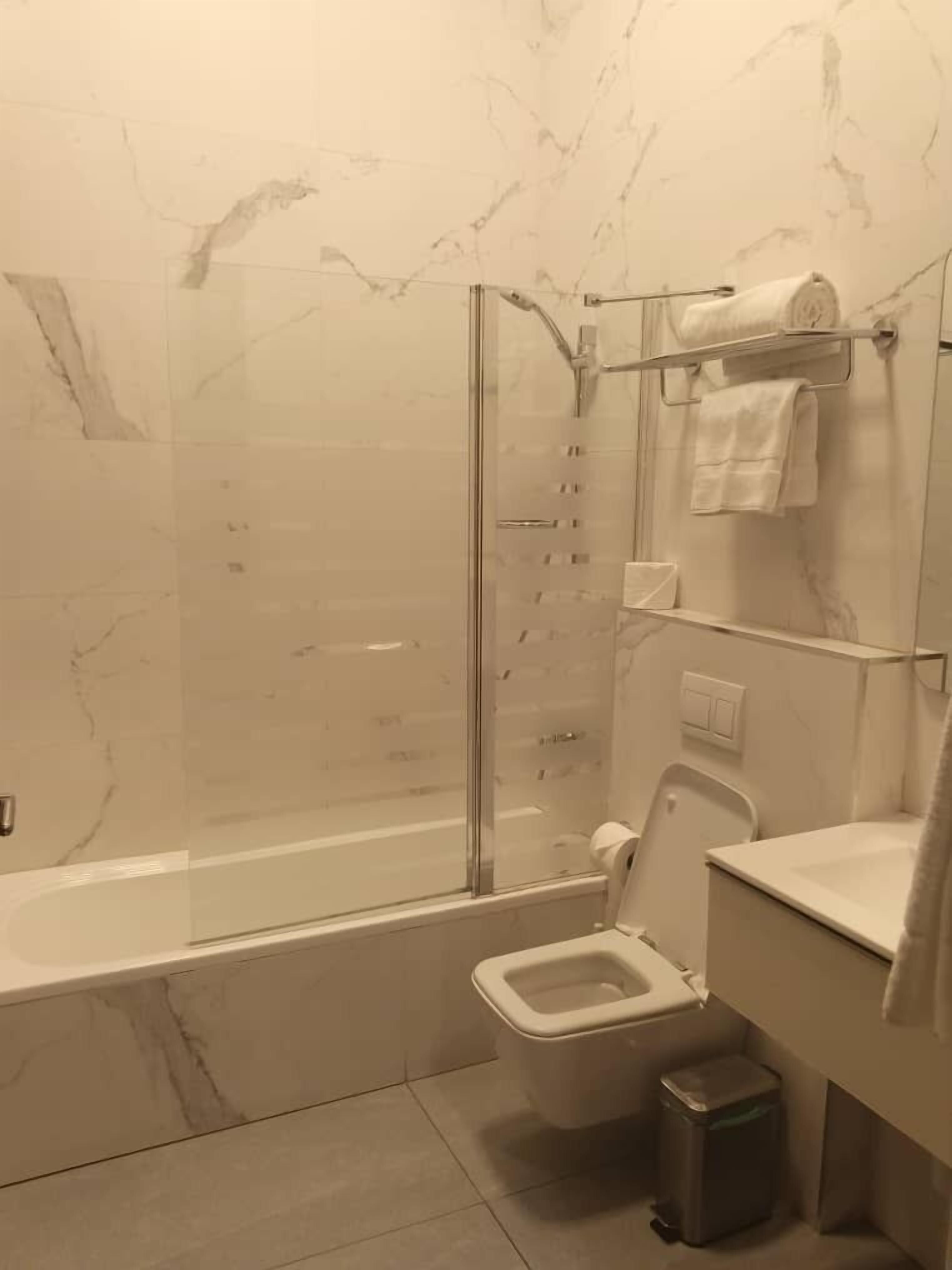 Baño con ducha de mampara de vidrio, inodoro, lavamanos y cubo de basura.