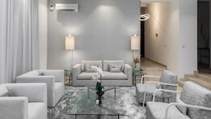 A modern living room with a grey sofa, white armchairs, a glass coffee table, and a grey textured wall. - Clayhall By SRS (Lagos)