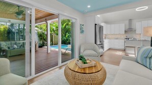 Un salon moderne avec vue sur la piscine, une cuisine dotée de meubles blancs et un coin repas.