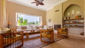 A living room with a sofa set, a coffee table, and two wooden chairs with metal frames. - Nyssa, swimming pool, pétanque, garden & staff (Marrakech)