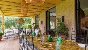 A covered outdoor dining area with a brick wall, wicker furniture, and potted plants. - Nyssa, swimming pool, pétanque, garden & staff (Marrakech)