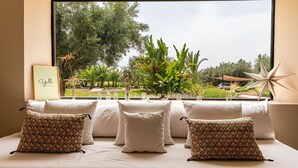 A hotel room with a large window, a bed with white linens, and decorative pillows. - Nyssa, swimming pool, pétanque, garden & staff (Marrakech)