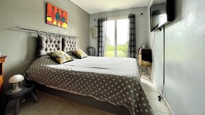 A bedroom with a bed, a TV, a painting, and a window with curtains. - Detached house, fully fenced, swimming pool, bowling green, dogs welcome. (La Bezole)