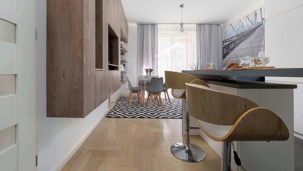 Een moderne keuken met een houten accentmuur, een eethoek met een vloerkleed met dessin en een keukeneiland met barkrukken.