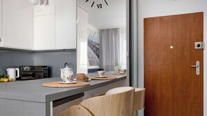 Een moderne keuken met een magnetron, waterkoker, kopjes en een houten stoel.