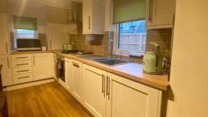 A modern kitchen with white cabinets, a wooden countertop, a sink, a kettle, and a window with a view of the outside. - Elliot Cottage Your Retreat in Heart of Peebles (Scottish Borders)