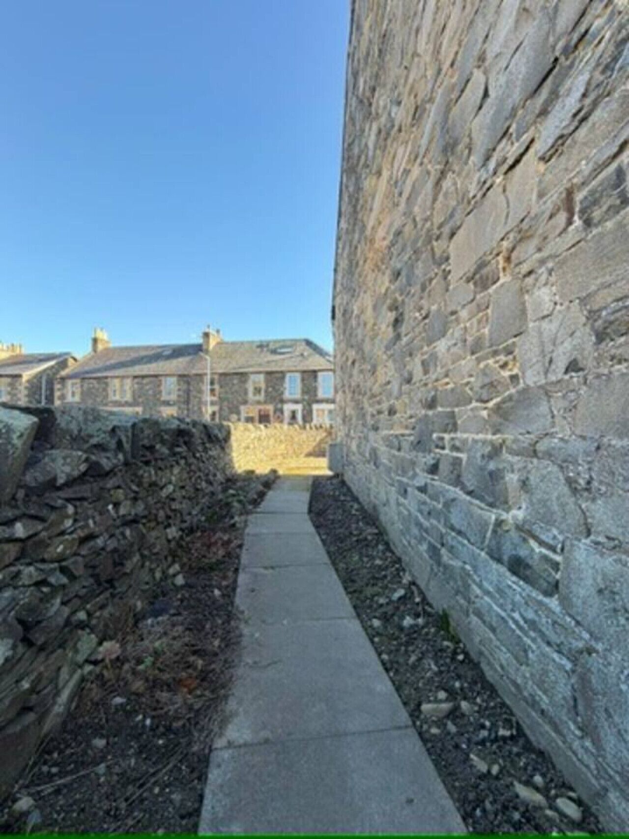 Un estrecho sendero de piedra que lleva a un muro de piedra, con un edificio al fondo.