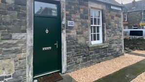 A stone building with a green door, a small window, and a sign indicating a 'Cottage'. - Elliot Cottage Your Retreat in Heart of Peebles (Scottish Borders)