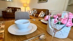 A dining area with a wooden table set for two, including a bowl, plates, cutlery, and a glass with flowers. - Elliot Cottage Your Retreat in Heart of Peebles (Scottish Borders)