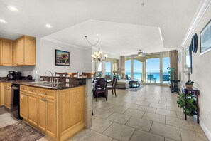 A spacious kitchen with wooden cabinets and a granite countertop, leading to a dining area with a view of the ocean. - 🌞🌊Gulf and Sound Views | Resort Amenities | Portofino Island Resort 3-1209 (Pensacola Beach)