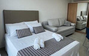 A hotel room with a bed, a grey sofa, and a mirror reflecting a chair. - ACQUA BEACH RESIDENCE, a paradise 4 minutes from Tamandaré/Carneiros Beach (Tamandaré)