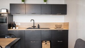 Une cuisine de taille réduite, avec des meubles de couleur sombre, un plan de travail en bois et un petit évier.