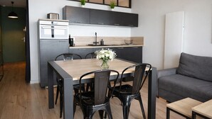 Une cuisine moderne avec des meubles de rangement sombres, une table à manger en bois et des chaises noires.