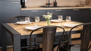 Une table à manger dressée avec de l’assiette blanche, des verres à vin et un vase rempli de fleurs blanches.