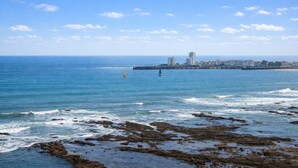 Une vue sur la côte, avec un rivage rocheux, une mer calme et des bâtiments situés au loin.