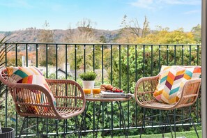 Two wicker chairs with colorful cushions on a balcony with a view of hills and trees. - Rigg & Rest - Central Bowness, Balcony & Parking (Bowness-on-Windermere)